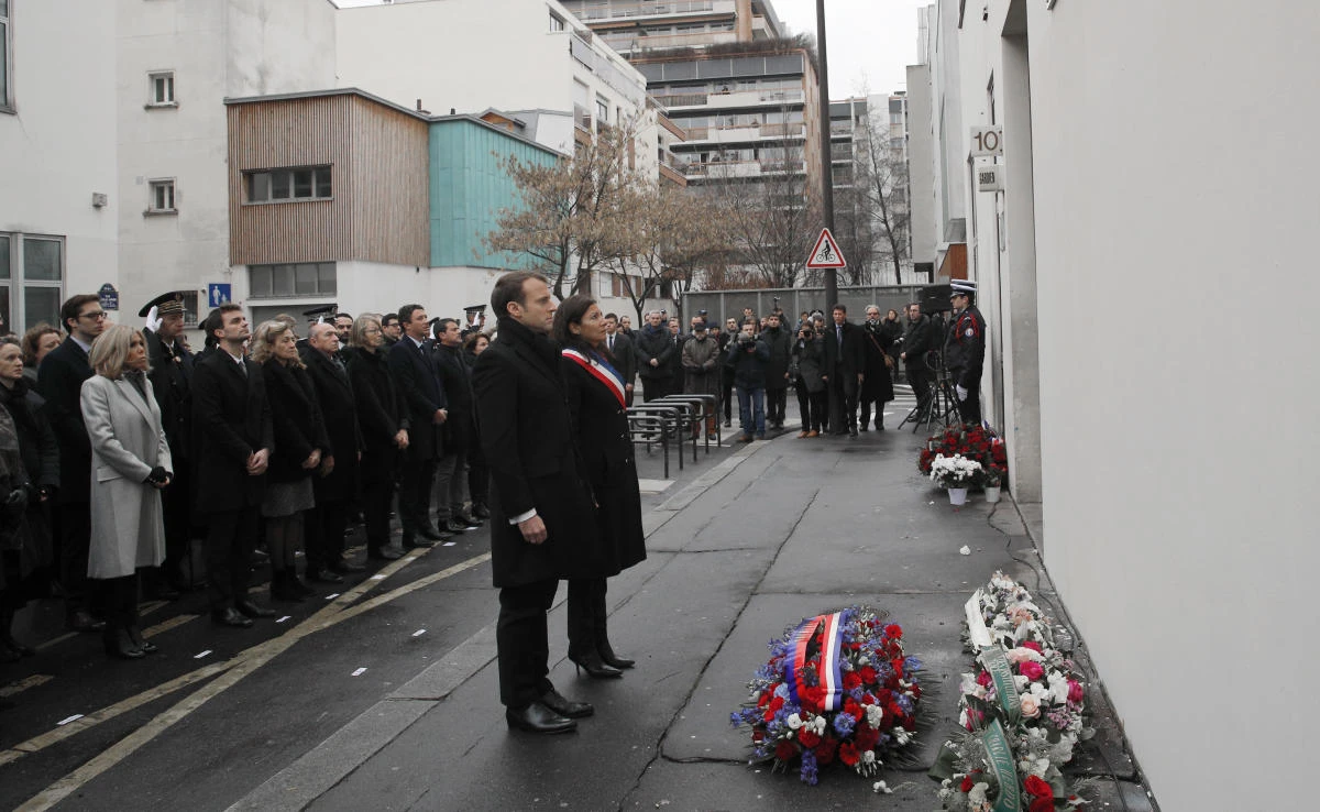 French President Emmanuel Macron, center and Paris mayor Anne Hidalgo observe a minute of silence outside the satirical newspaper Charlie Hebdo former office, to mark the third anniversary of the attack, in Paris, Sunday, Jan. 7, 2018. (Pool via AP)