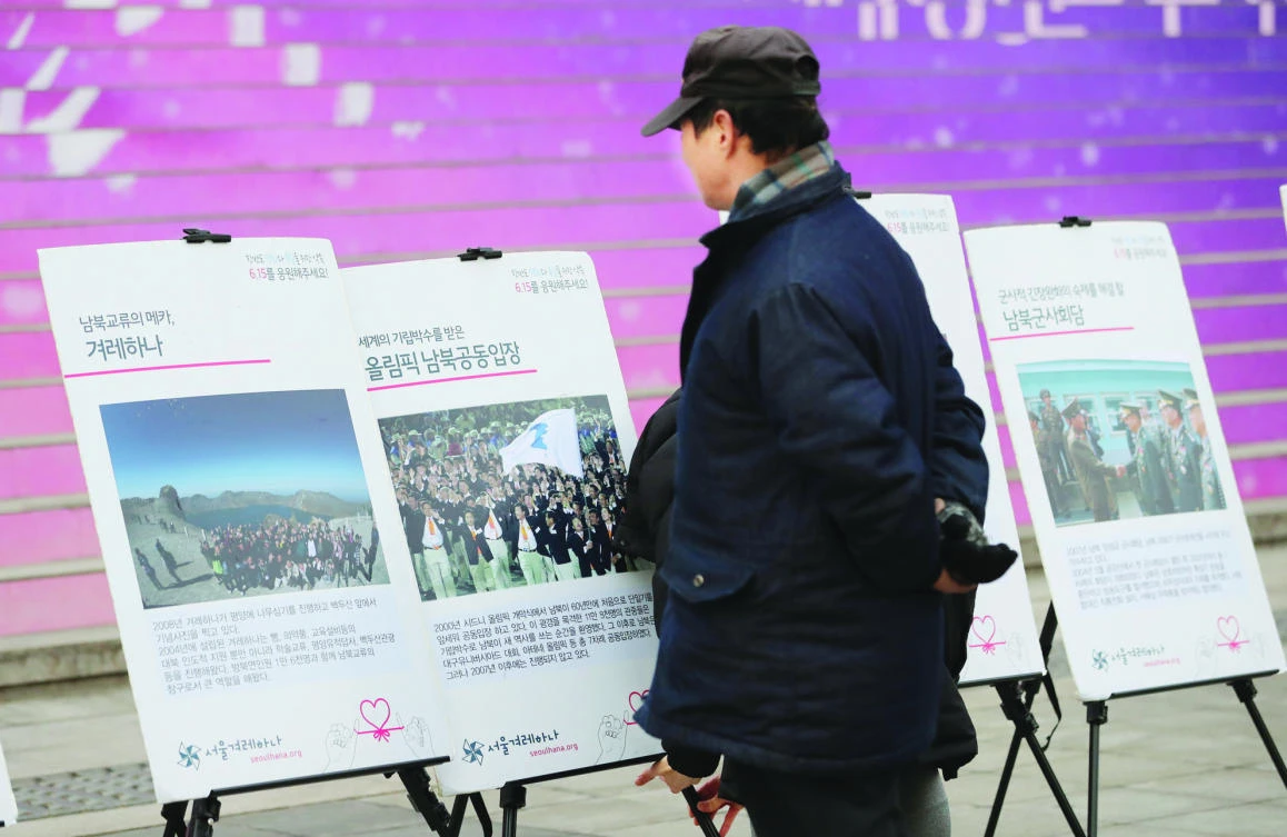 A man watches a photo, second from left, showing athletes from North and South Korea march together, led by a unification flag during the 2000 Sydney Olympics, displayed at a street campaign ahead of two Koreas talks in Seoul Monday. (AP)