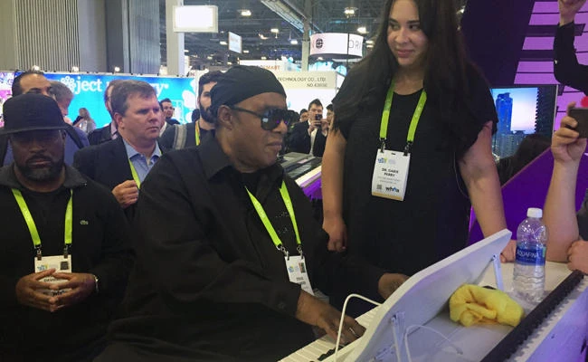 Musician Stevie Wonder plays a "smart" piano, an internet-connected device designed to teach people how to play, while piano teacher Gabie Perry stands next to him at The One Music Group's CES booth in Las Vegas. (AP Photo/Matt O'Brien)