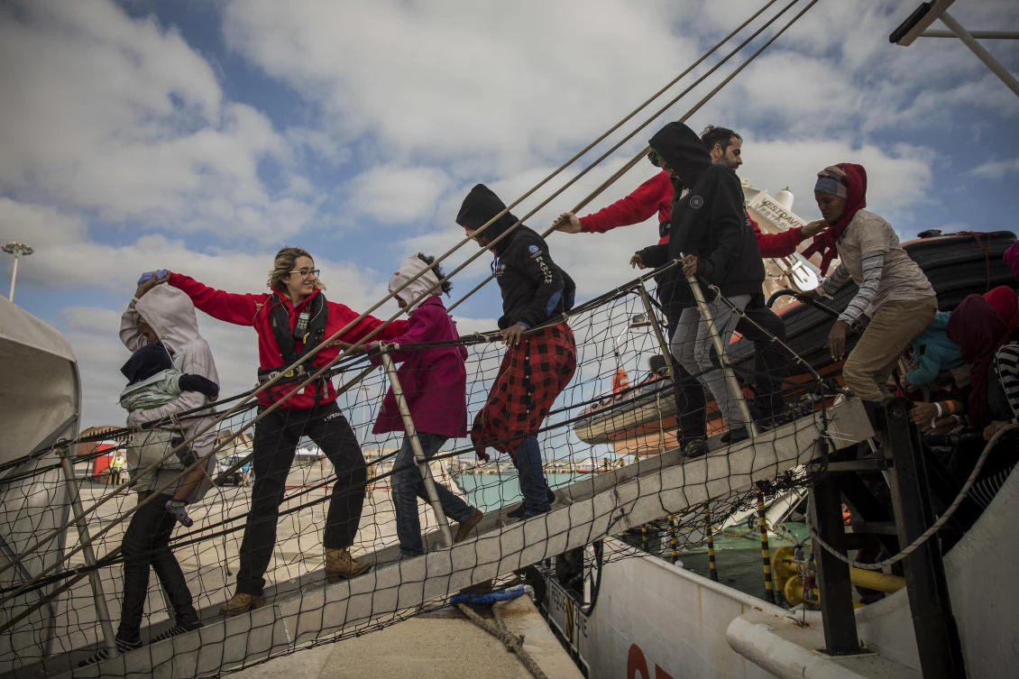 Aid workers from the Spanish NGO Proactiva Open Arms help refugees and migrants to disembark from the rescue vessel, at the port of Pozzallo, Italy. (AP)