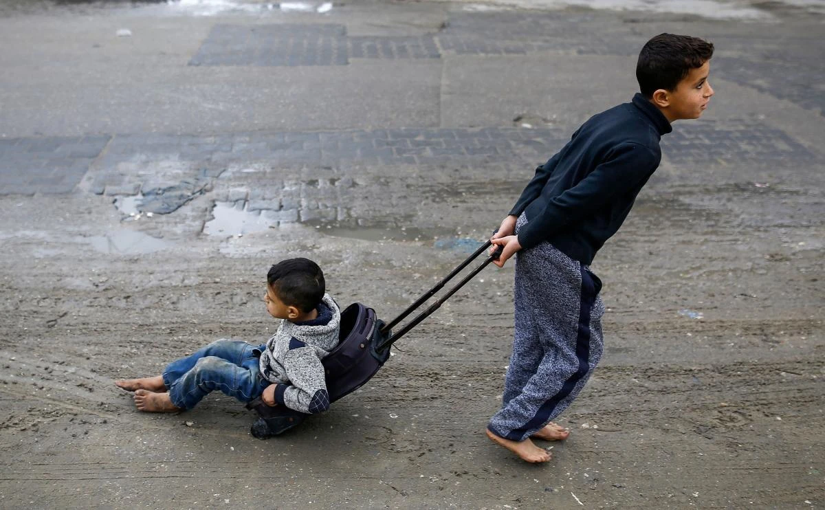 A Palestinian boy pulls his brother as he sits in a wheeled-suitcase as he walks down a street in a refugee camp in Gaza City on January 23, 2018. The United Nations Relief and Works Agency for Palestine Refugees (UNRWA), set up after the 1948 creation of Israel that drove huge numbers of Palestinians from their homes, faces what the UN has described as the “most severe” crisis in its history as the US held back $65 million that had been assigned for it two weeks after President Donald Trump threatened future payments. (AFP/Mohammed Abed)