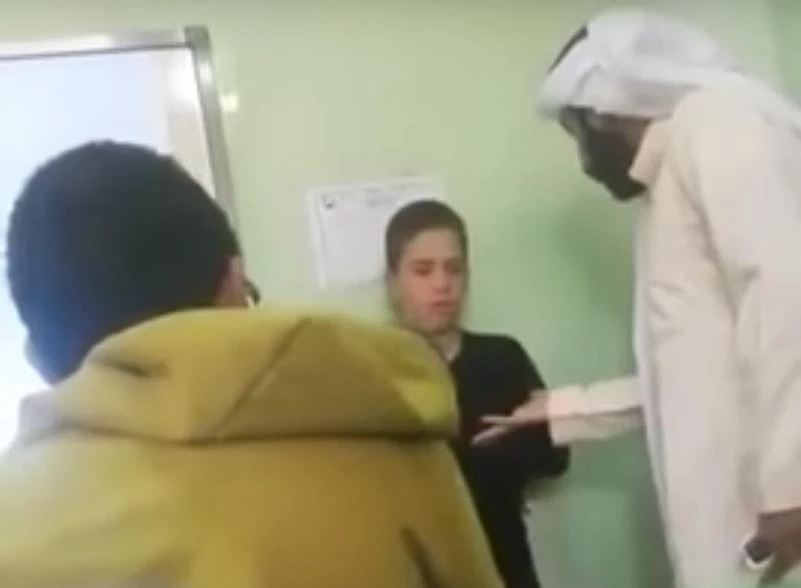 A Saudi private elementary school teacher in Al-Ahsa province holding a wooden stick with one hand and pushing a student into the wall with the other. (video grab)
