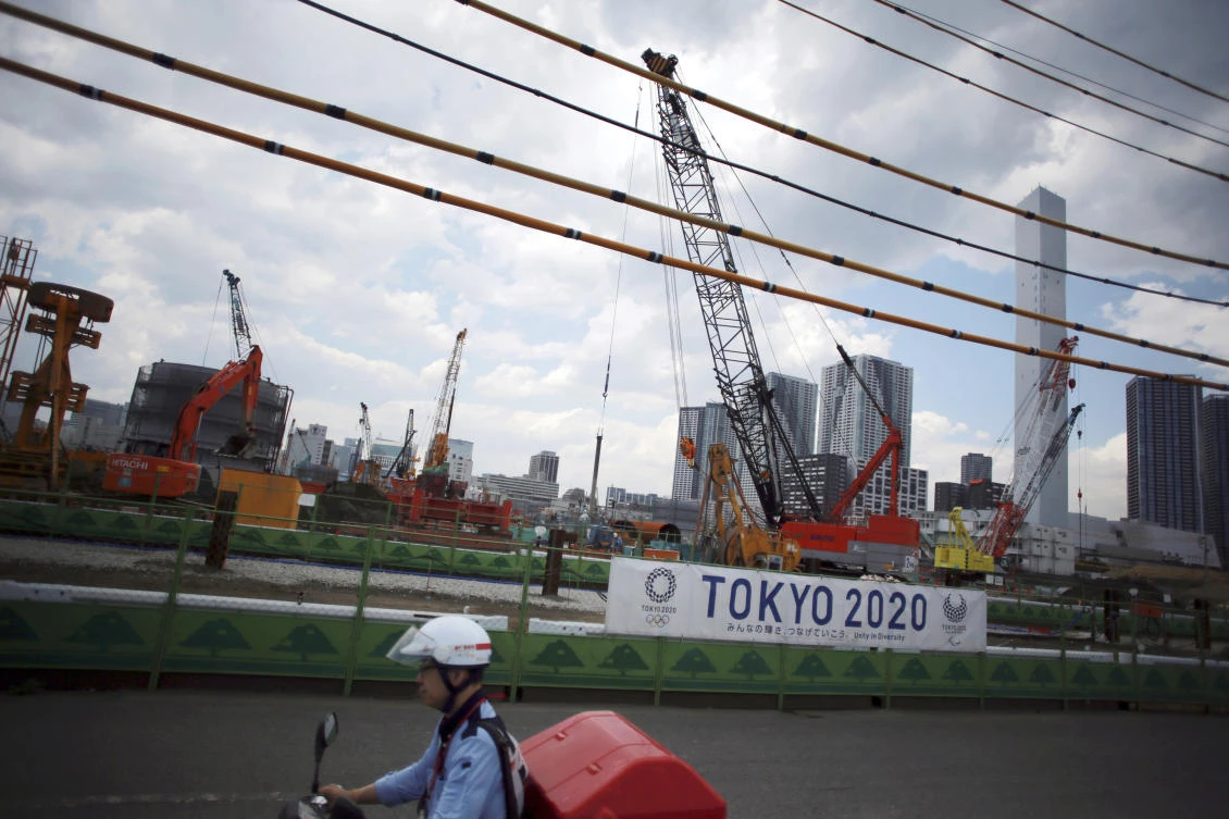 Above, a postman rides a motorcycle past the construction site of the athlete's village for the 2020 Tokyo Summer Olympics at Tokyo's Harumi. Tokyo’s winning bid in 2013 for the 2020 Olympics was listed at ¥730 billion, about one-third of the list price now. (AP)