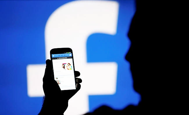 A man is silhouetted against a video screen with an Facebook logo as he poses with an Samsung S4 smartphone in this photo illustration, in this August 14, 2013 file photo. (REUTERS)