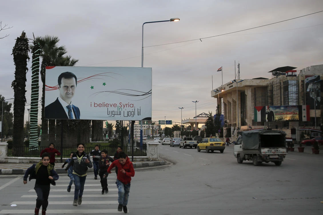 In this file photo, Syrian children cross a street in front of a banner showing President Bashar Assad in Syria. According to Tareq, residents live in near-constant “fear of being arrested or evicted”.(AP)