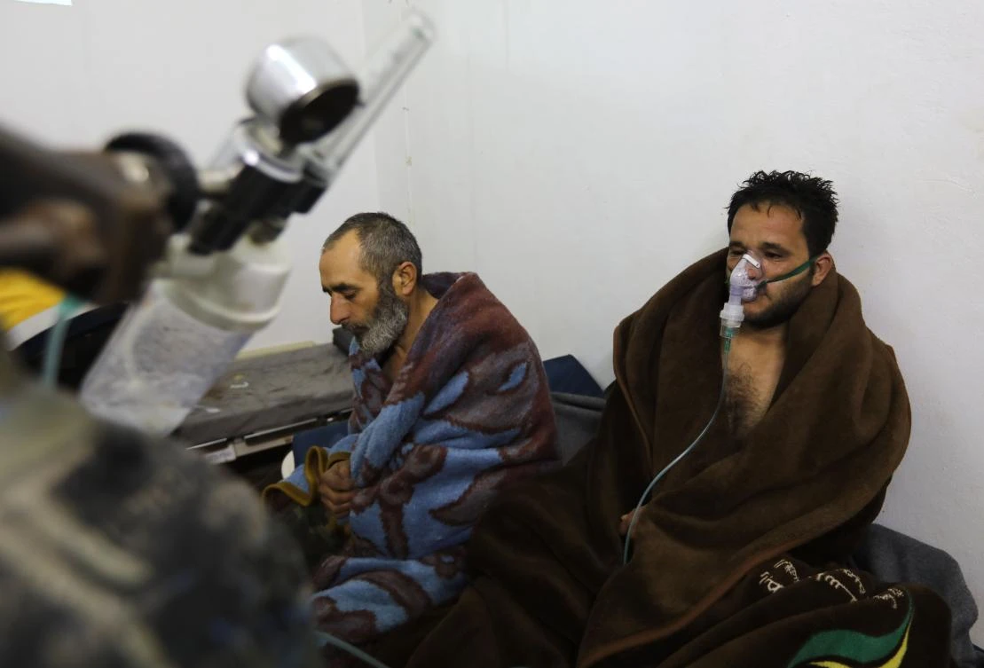 Syrians reportedly suffering from breathing difficulties following Syrian regime air strikes on the northwestern town of Saraqeb rest around a stove at a field hospital in a village on the outskirts of Saraqeb, due to the lack of hospitals in the town, on February 4, 2018. (AFP)