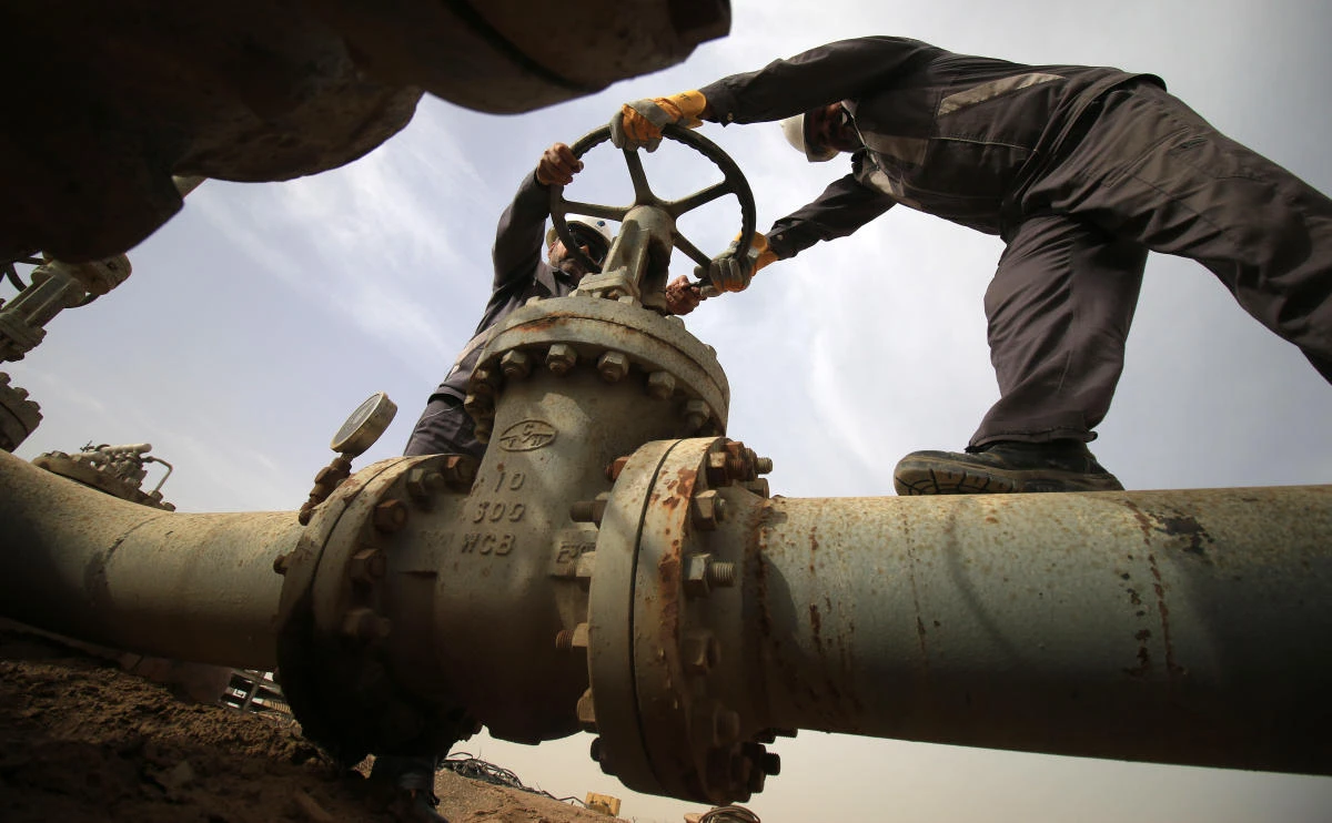 Iraqi oil technicians turn a valve at a gas installation as flames resulting from the burning of excess hydrocarbons rise in the background at the Nahr Bin Omar natural gas field, north of the southern Iraqi port of Basra on January 22, 2018. Iraq will is expected to sign a memorandum of understanding with US energy company Orion on January 22 to tap gas at the oil field in the south of the country, the petroleum ministry said.