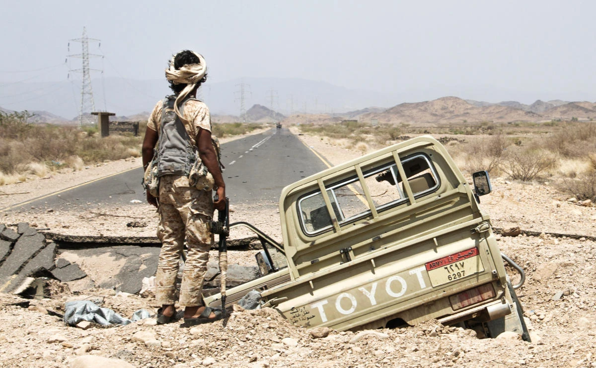 A Yemeni fighter loyal to the Saudi-backed Yemeni president stands next to an army Toyota pickup truck as it lies in hole on the road. (AFP)