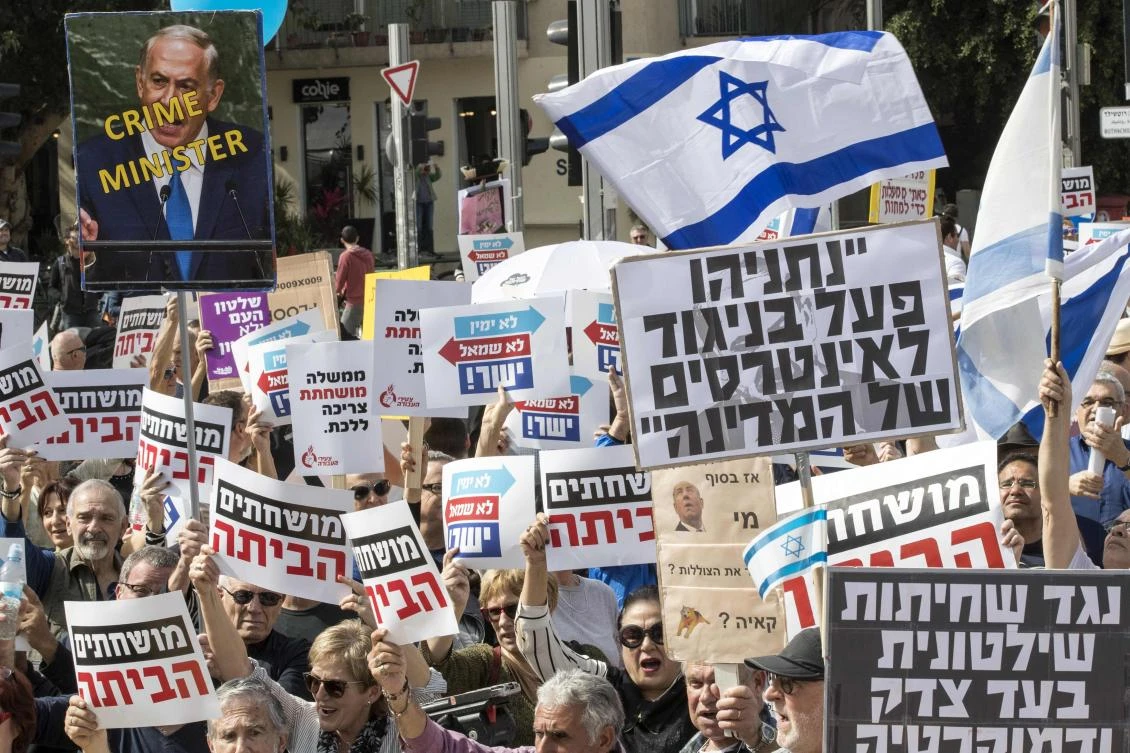 Israeli protesters raise a sign reading in Hebrew “Netanyahu acted against Israel’s interest” (C-R), during a demonstration against Prime Minister Benjamin Netanyahu in the wake of police recommendations to indict corruption, in Tel Aviv on Feb.16, 2018. (AFP)