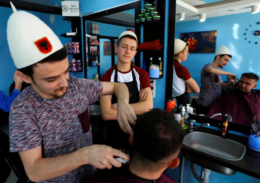 A barber wears a traditional hat with an Albanian flag ahead of 10-year independence celebrations in Kacanik. Ethnic divisions and widespread unemployment have made Kosovo's journey to nationhood a difficult one. (Reuters)