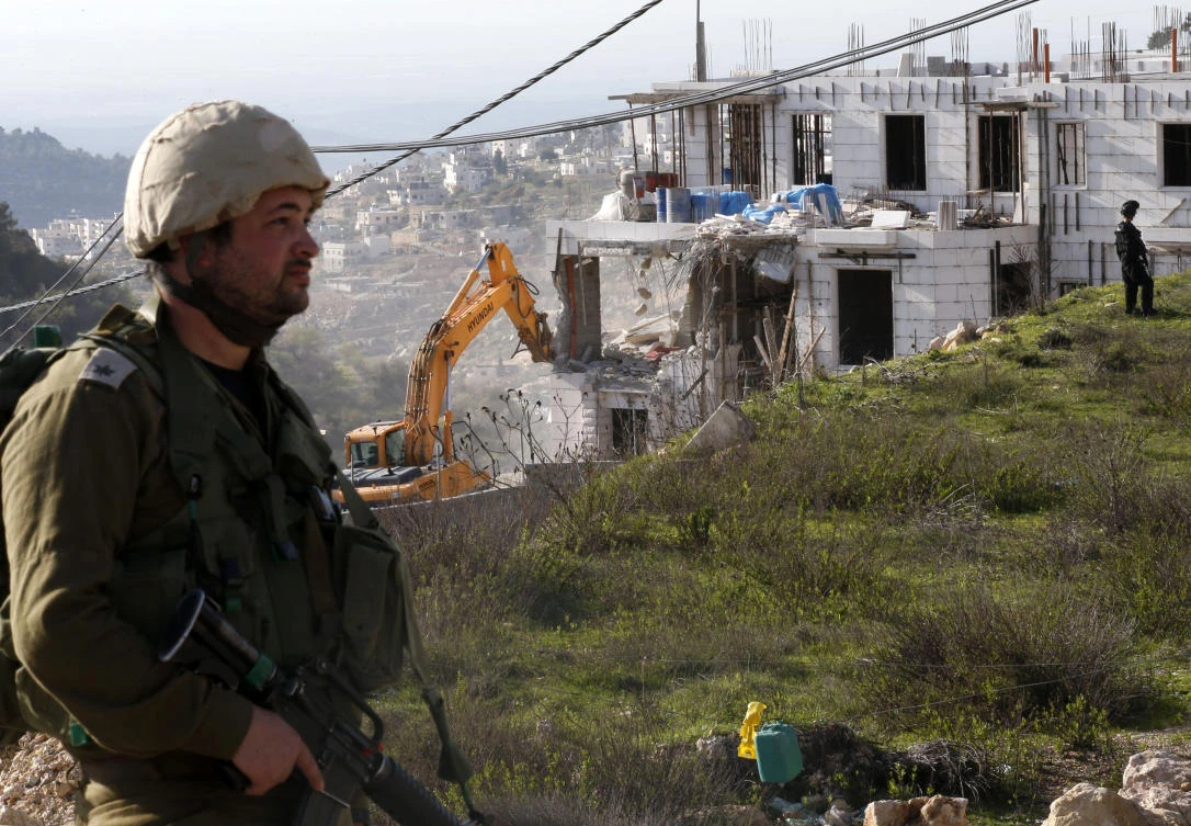 Israeli soldiers and border police stand guard as Israeli hydraulic shovels demolish a Palestinian building near road 35, north of the occupied West Bank city of Hebron in the so-called “Area C” on February 14, 2018. (Hazem Bader/AFP)