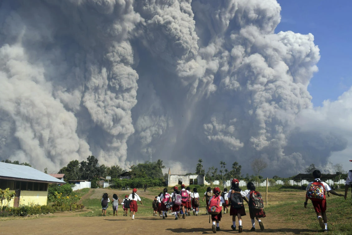 School children walk as Mount Sinabung erupts in Karo, North Sumatra, Indonesia, Monday, Feb. 19, 2018. Rumbling Mount Sinabung on the Indonesian island of Sumatra has shot billowing columns of ash more than 5,000 meters (16,400 feet) into the atmosphere and hot clouds down its slopes. (AP/Sarianto)
