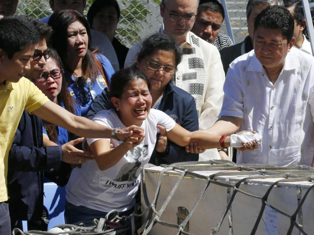 Jessica, centre, and Jojit Demafelis, left, siblings of Joanna Demafelis react as the wooden casket of her remains arrives at the Ninoy Aquino International Airport. (AP)