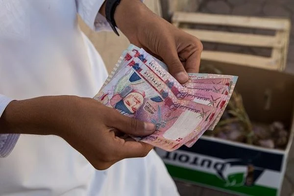 A man carries a stack of Omani riyals. (Shutterstock)