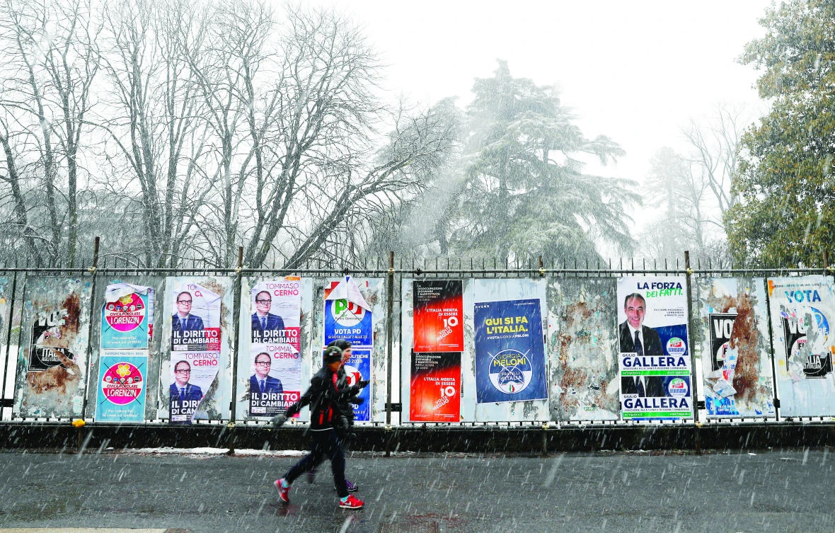 Two women walk past electoral posters for Italy’s general elections, in Milan on Saturday. (AP)