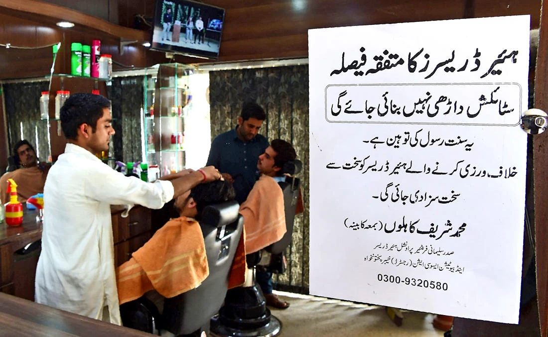 Pakistani hairdressers work at their stations beside a notice sign of the the Sulemani Hairdressers Association that reads “All hairdressers by unanimous decision have decided not to offer their services for clients wishing for stylish beards. It is an insult of Sunnah of Prophet. Violators will be given a harsh punishment,” in Peshawar on March 6, 2018.