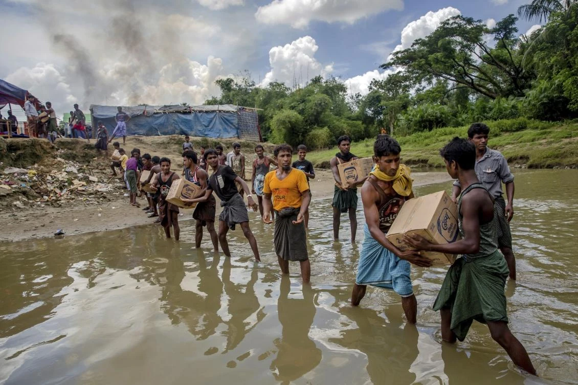 Rohingya Muslims carry food items across from Bangladesh towards no man's land where they have set up a refugee camp, as smoke rise from fire across the border in Myanmar, in Tombru. (AP)