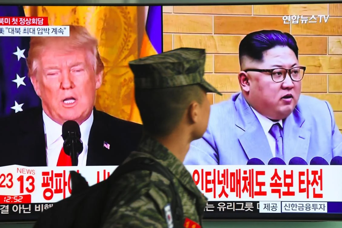 A South Korean soldier walks past a television screen showing pictures of US President Donald Trump (L) and North Korean leader Kim Jong Un at a railway station in Seoul on March 9, 2018. (AFP)