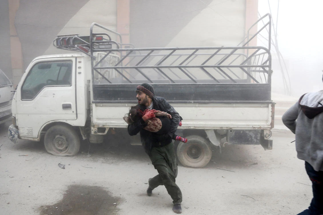 A man carries a child as he flees from reported Syrian air force strikes that hit the opposition-held town of Saqba, in the besieged Eastern Ghouta region on the outskirts of the capital Damascus. (AFP/file)