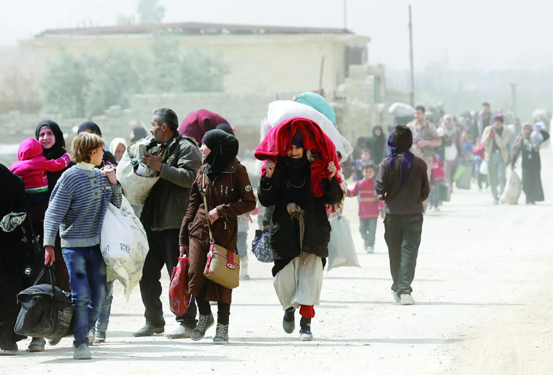 Syrians from opposition-held Eastern Ghouta walk through a regime-controlled corridor in Hawsh Al-Ashaari, east of the Eastern Ghouta town of Hamouria, on the outskirts of the capital Damascus, after escaping the enclave on Thursday. (AFP)