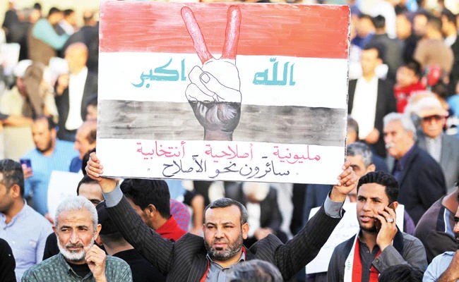 An Iraqi supporter of Moqtada Al-Sadr raises a sign showing the colors of the Iraqi flag superimposed on a hand flashing the victory gesture with
a caption in Arabic reading at the bottom ‘million-man march, reformist, electoral, walking towards reform,’ during a demonstration
in Baghdad against corruption in the Iraqi government on March 2. (AFP)