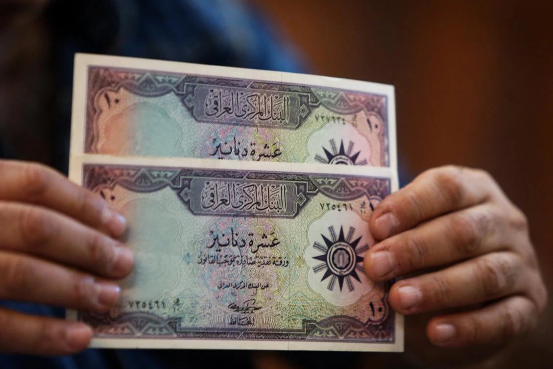 A man holds up preserved specimens of Ten Iraqi Dinar banknotes, during a historical relic auction at the Moudallal cafe, Arabic for “pampered,” in the Iraqi capital Baghdad on March 3, 2018. (AFP)