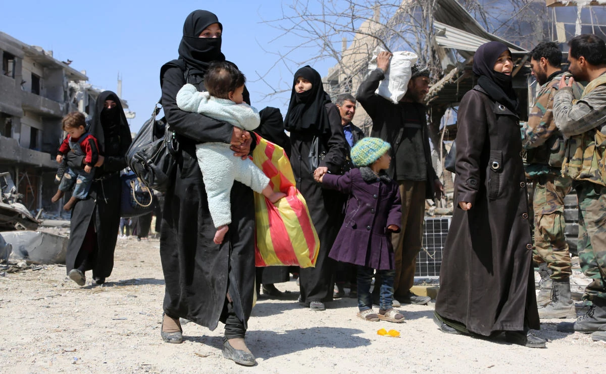 Syrian women and children walk past government soldiers as they evacuate from the town of Jisreen in the southern Eastern Ghouta, on the eastern outskirts of the capital Damascus, on March 17, 2018. (AFP)