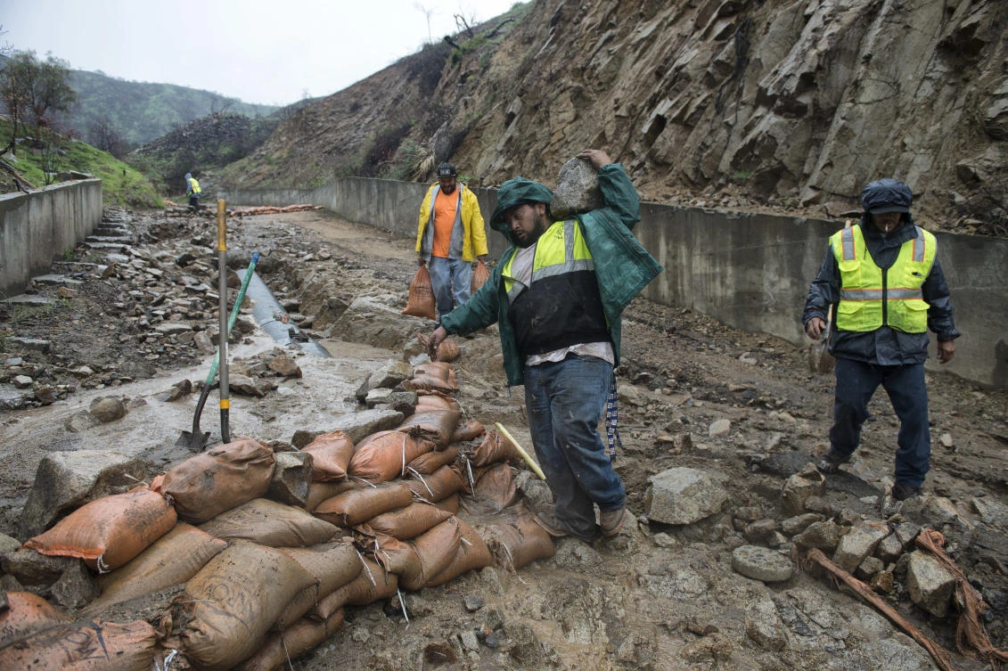 Workers place sandbags on a washed-out driveway on La Tuna Canyon Road in Sun Valley, California. A strong Pacific storm dropped heavy rain Wednesday on a swath of California where thousands of people have been evacuated because of the threat of debris flows and mudslides from wildfire burn areas. (Los Angeles Daily News via AP)