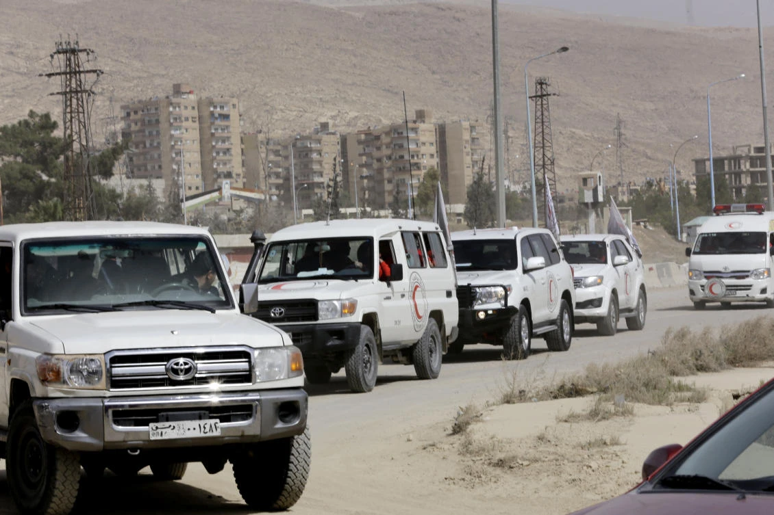 Red Crescent vehicles wait at the entrance of Harasta in Eastern Ghouta, on the outskirts of Damascus, on March 22, 2018, after a deal was struck with the rebels in the area to evacuate the town. The deal to evacuate mainly members of the hard-line Islamist rebel group Ahrar Al-Sham and their families was announced on March 21 and brokered by regime ally Russia. (AFP/Louai Beshara)