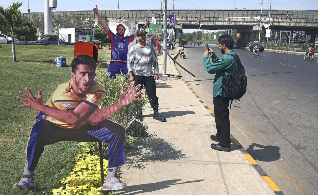 A man takes a photo of his friend standing beside a cut-out of a cricket player displayed along the roadside in preparation of the upcoming Pakistan Super League final in Karachi, Pakistan, Saturday, March 24, 2018. (AP)