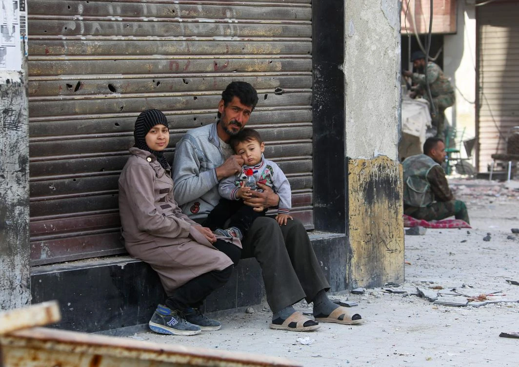 A Syrian man sits with his family at the entrance of a shrapnel riddled shop near government forces in the Eastern Ghouta town of Kafr Batna, on the northeastern outskirts of Damascus, on March 20, 2018. Government forces took control of Kafr Batna in the southern pocket of Eastern Ghouta that was held by the Faylaq Al-Rahman rebel group, on March 17. (AFP)