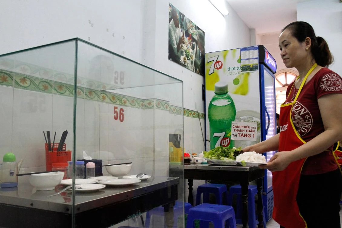 In this photograph taken on March 20, 2018, a waitress carries dishes to customers next to the glass-encased table where former US President Barack Obama sat at for a meal with chef Anthony Bourdain at Bun Cha Huong Lien restaurant. (AFP)