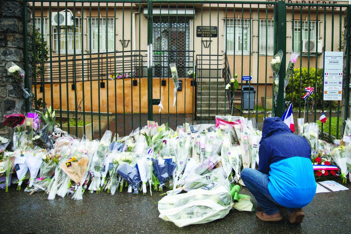 A man places flowers at the main gate of the police headquarters in Carcassonne on Saturday, following an attack on a supermarket in the south of France on Friday. (AP)