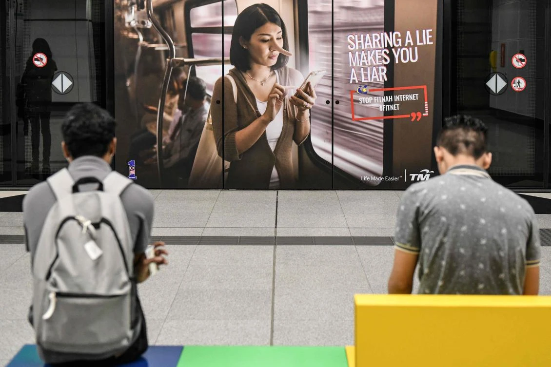 Commuters wait for a train in-front of an advertisement reading ‘sharing a lie makes u a liar’ at a station in Kuala Lumpur. The Malaysian government proposes combating ‘fake news’ by sending offenders to jail for 10 years. (AFP)