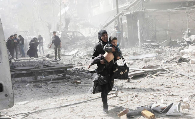 A Syrian woman holds a child and runs for cover following Syrian government air strikes on the Eastern Ghouta rebel-held enclave of Douma, on the outskirts of the capital Damascus, in this March 20, 2018 photo. (AFP)