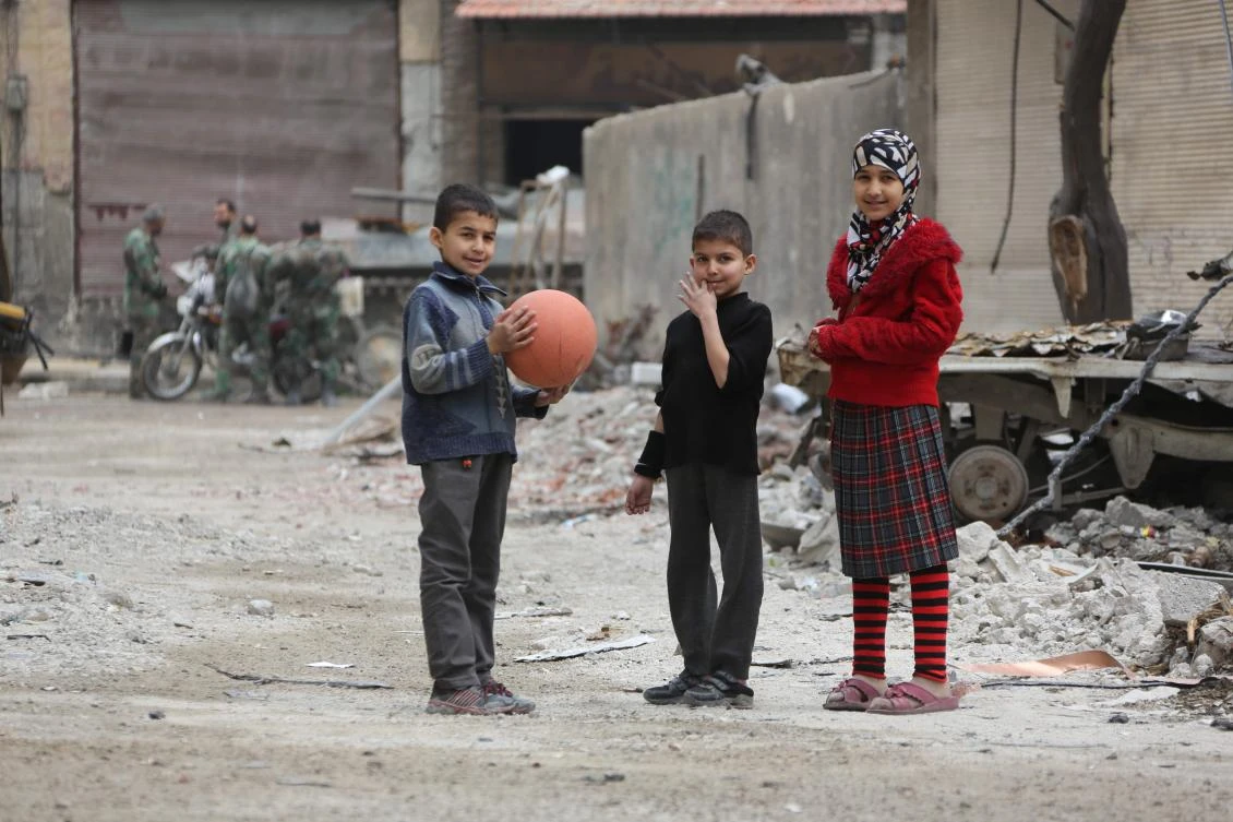 Syrian children stand in a street as one of them holds a basketball, in the town of Hazzeh in Eastern Ghouta, on the outskirts of the Syrian capital Damascus, on March 28, 2018. / AFP / STRINGER