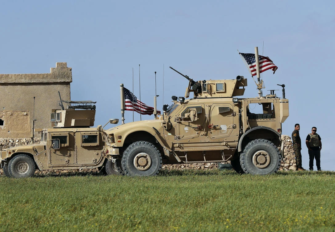 In this picture taken on Thursday, March 29, 2018, a fighter, second from right, of U.S-backed Syrian Manbij Military Council stands next to US humvee at a US troop’s outpost on a road leading to the tense front line between Syrian Manbij Military Council fighters and Turkish-backed fighters, at Halawanji village, north of Manbij town, Syria. (AP)