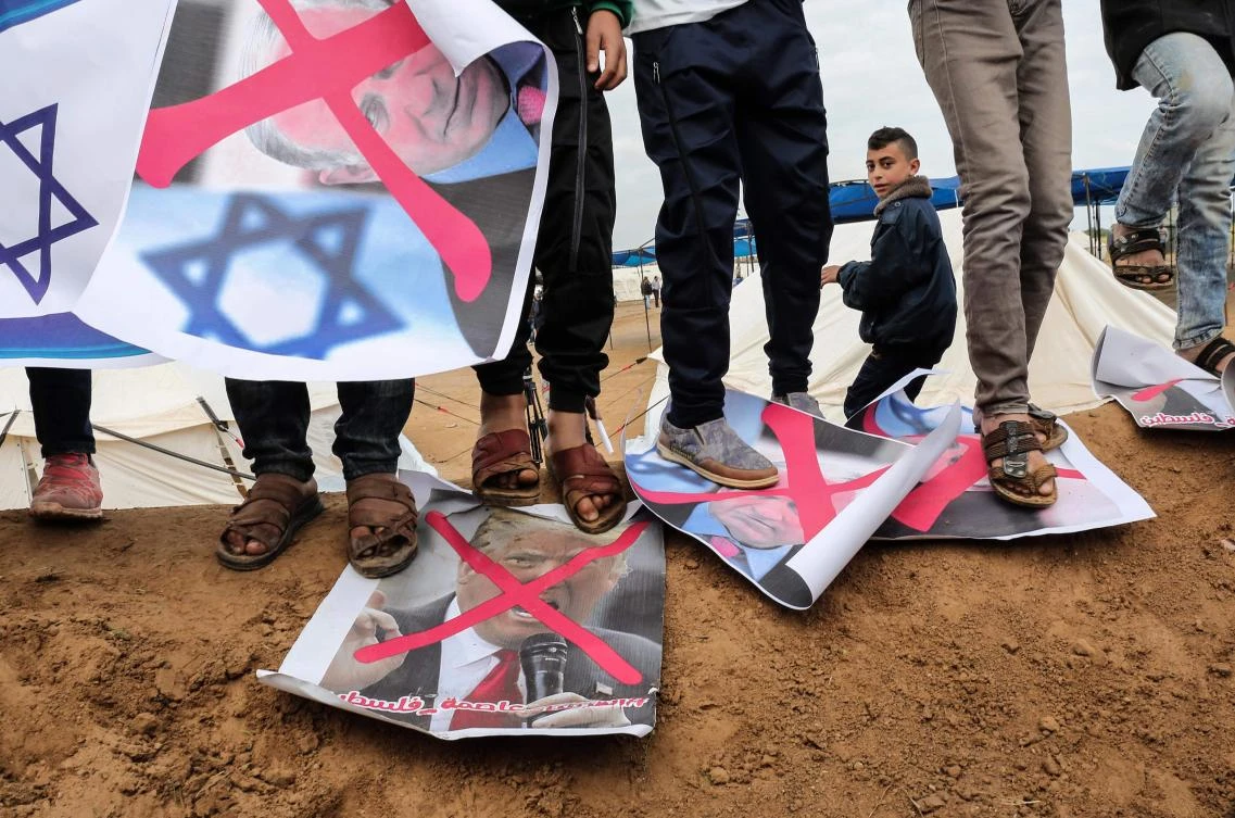 Palestinians step on crossed-out posters depicting Israeli Prime Minister Benjamin Netanyahu and US President Donald Trump during a tent city protest near Khan Yunis in the southern Gaza Strip. (AFP)