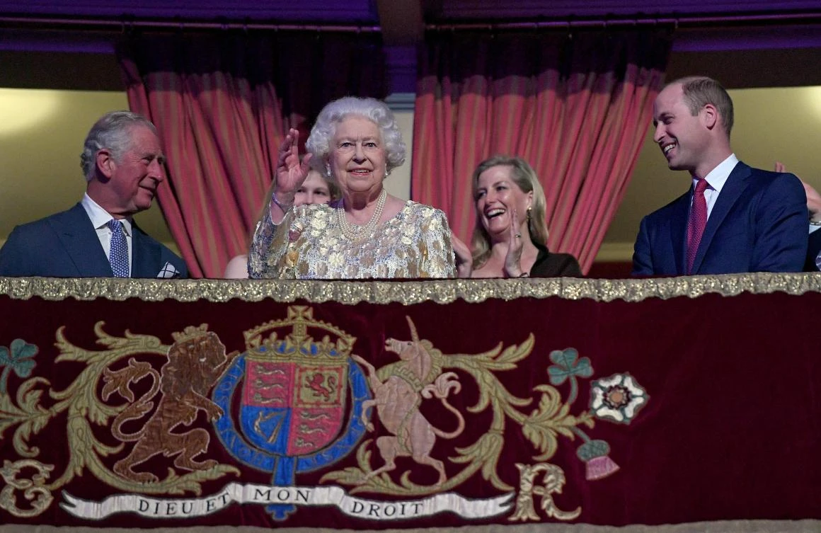 Britain's Queen Elizabeth II (centre L) waves to guests as her son Britain's Prince Charles, Prince of Wales (L) and grandson Britain's Prince William, Duke of Cambridge (R) react as she takes her seat ni the Royal box during The Queen's Birthday Party concert on the occassion of Her Majesty's 92nd birthday at the Royal Albert Hall in London on April 21, 2018. / AFP / POOL / Andrew Parsons