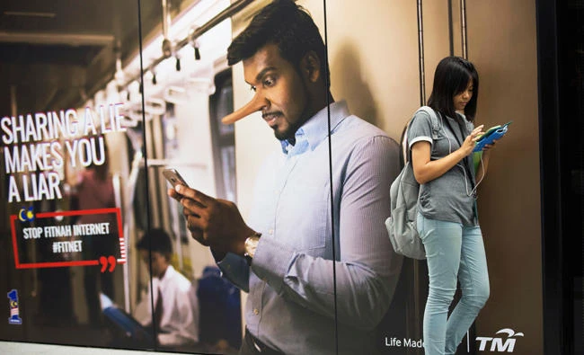 Commuter waiting for subway reading from her phone next to an advertisement discouraging the dissemination of fake news at a train station in Kuala Lumpur, Malaysia, in this March 29, 2018 photo. (AP)