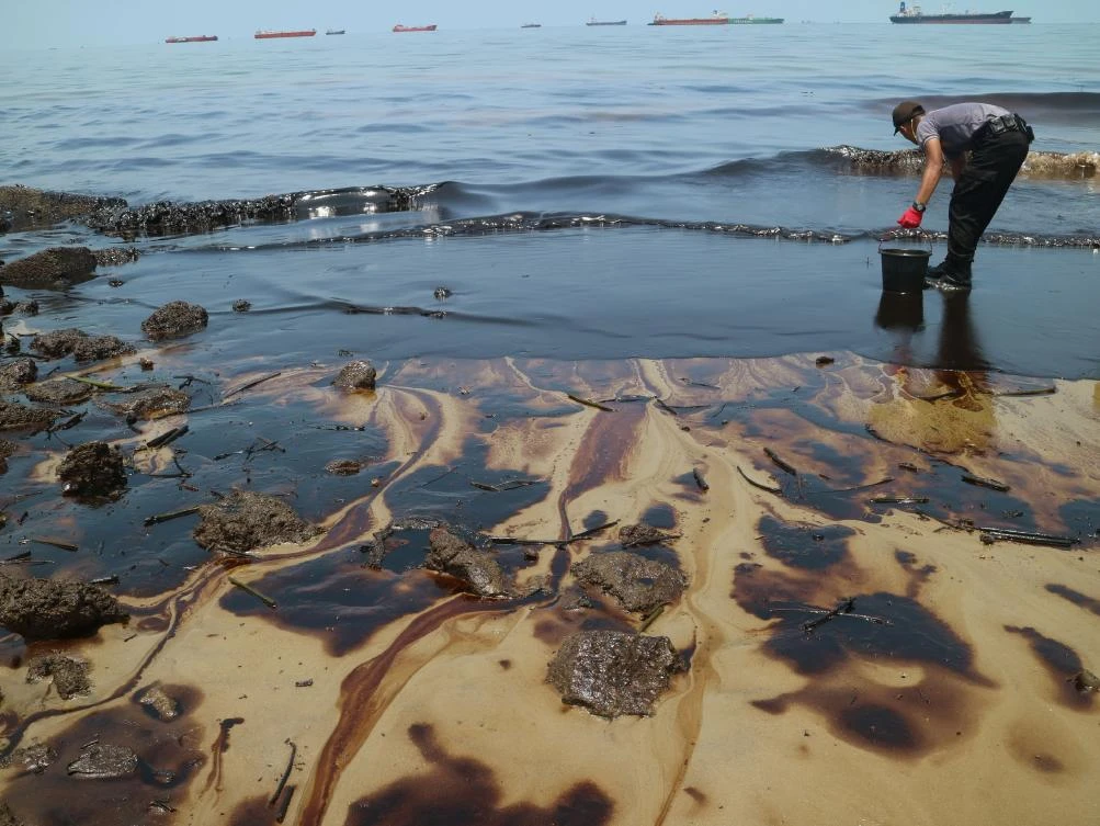 This picture taken on April 2, 2018 shows an Indonesian policeman trying to clean Benua Patra beach after a nearby oil spill in Balikpapan. (AFP)