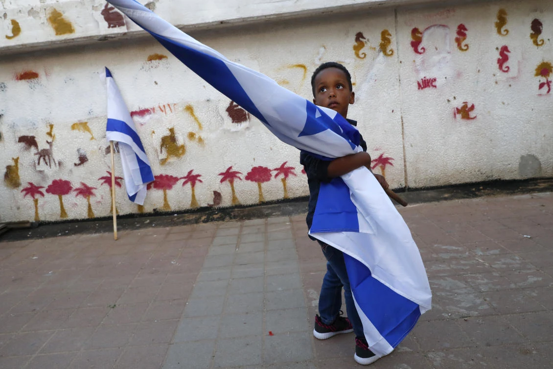 A boy holds the Israeli flag as African migrants and Israelis demonstrate in Tel Aviv on April 9, 2018 against the Israeli government’s policy to forcibly deport African refugees and asylum seekers. (Jack Guez / AFP)