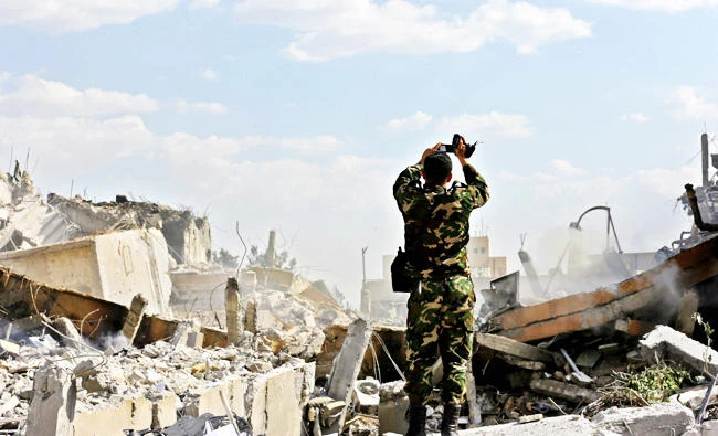 A Syrian regime soldier inspects the wreckage of a building in the Barzeh district, north of Damascus, during a press tour, following the Western strikes. AFP
