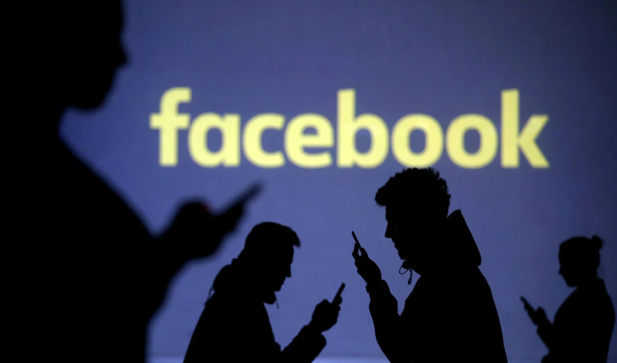 Silhouettes of mobile users are seen next to a screen projection of Facebook logo in this picture illustration taken March 28, 2018. (Reuters)