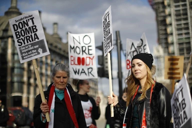 Protesters carry placards as they demonstrate against the UK's military involvement in Syria, outside the Houses of Parliament in central London on April 16, 2018. (AFP)