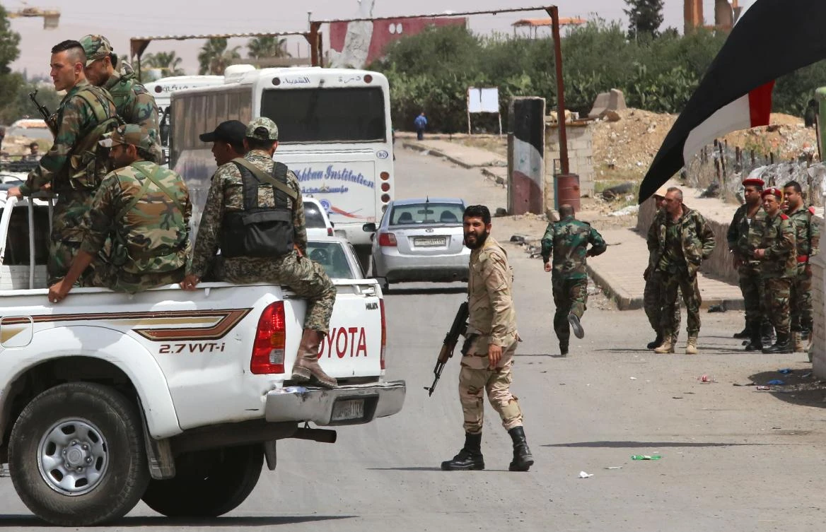 Pro-Syrian government forces gather around busses carrying Jaish Al-Islam fighters and their families from their former rebel bastion of Douma as they arrive at the Syrian government-held side of the Wafideen checkpoint on the outskirts of Damascus, after being evacuated from the last rebel-held pocket in Estearn Ghouta on April 9, 2018. (AFP /Youssef Karwashan)
