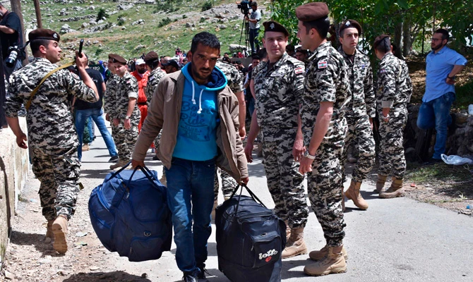 In this April, 18, 2018 file photo, a Syrian displaced man who fled the war in Syria carries his belongings past Lebanese soldiers as he prepares to return to his village of Beit Jinn in Syria, near the Lebanese-Syrian border, in Shebaa, southern Lebanon. (AP Photo/Ziad Choufi)