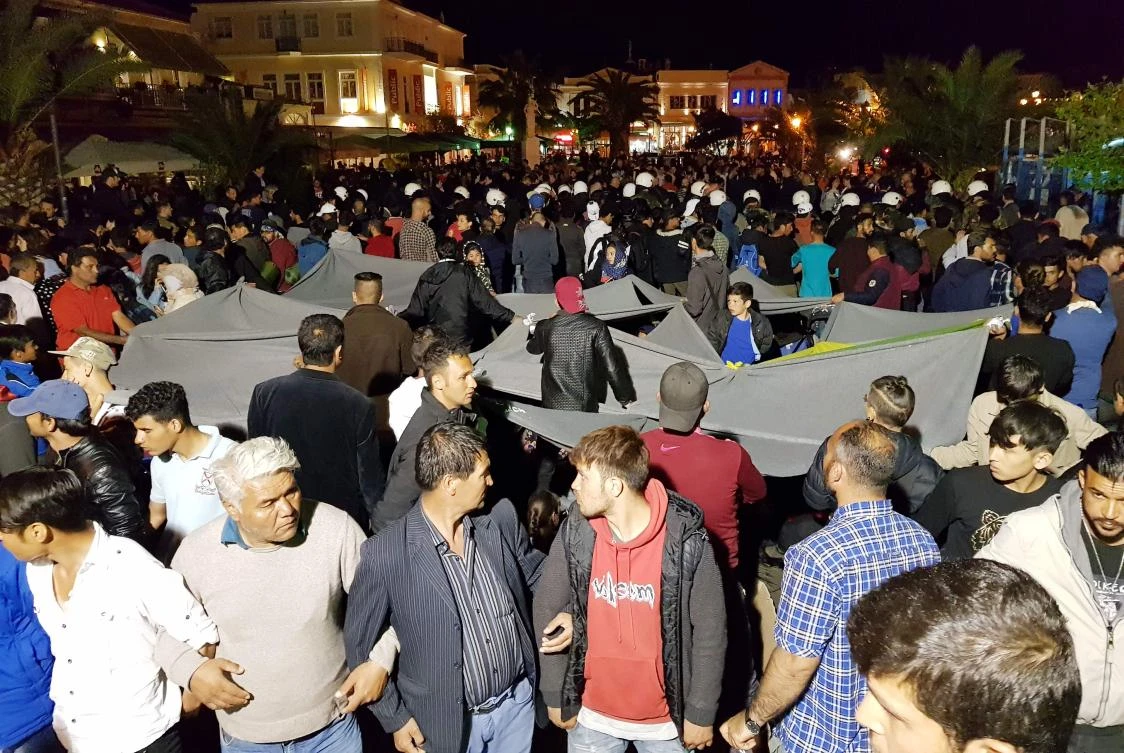 Migrants link their hands and hold blankets to protect their families as riot police try to keep away local protesters at the town of Mytilene on the island of Lesbos late on April 22, 2018. A far-right group launched a violent attack overnight on migrants staging a sit-in protest on the Greek island of Lesbos, injuring around a dozen people, police said on April 23. (AFP)