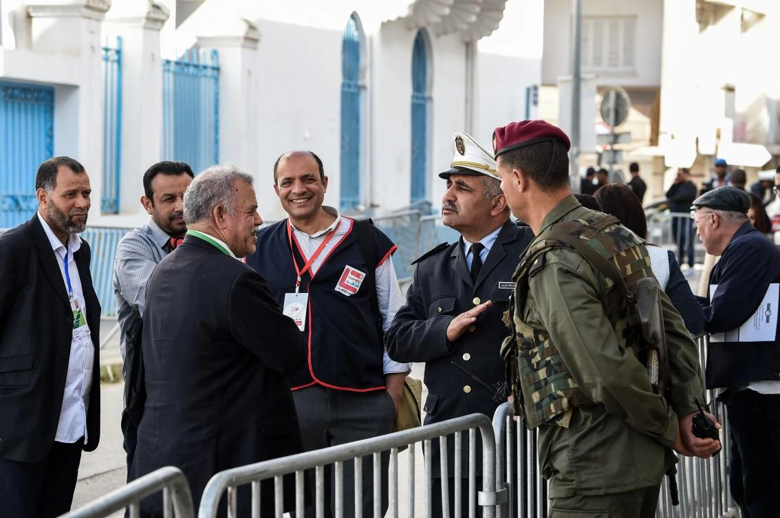 A Tunisian election observer (2nd-L) speaks with a policeman (C) as a soldier on guard (R) stands next to them, outside a municipal elections polling station for the police and military in the capital Tunis on April 29, 2018, during a special voting round for them ahead of the broader vote scheduled for May 6. (AFP/Fethi Belaid)