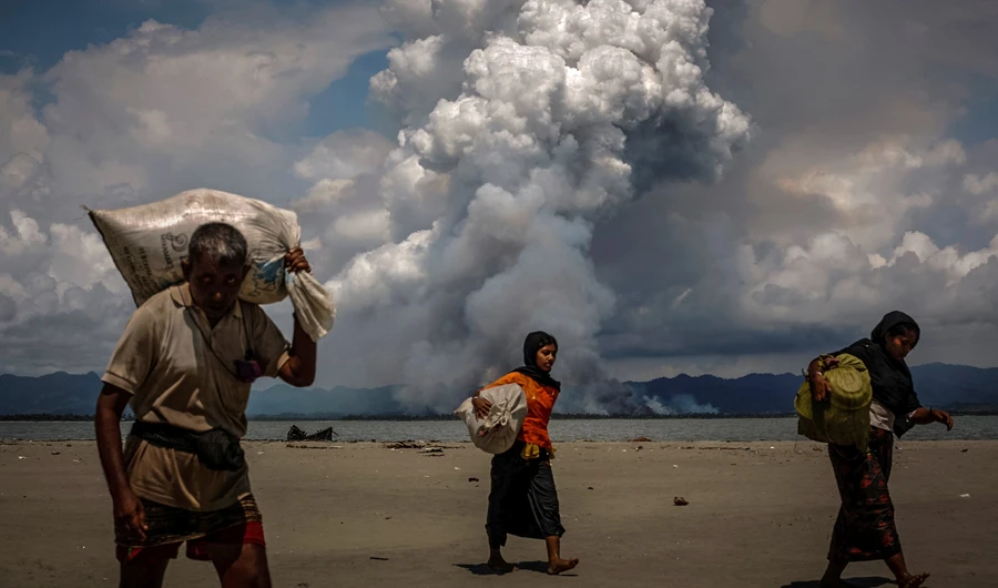 Smoke is seen on the Myanmar border as Rohingya refugees walk on the shore after crossing the Bangladesh-Myanmar border. (Reuters)